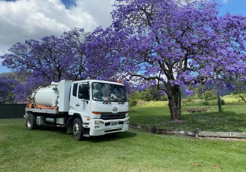 VACIT 120 WSJ UD vacuum truck parked beside a flowering jacaranda tree