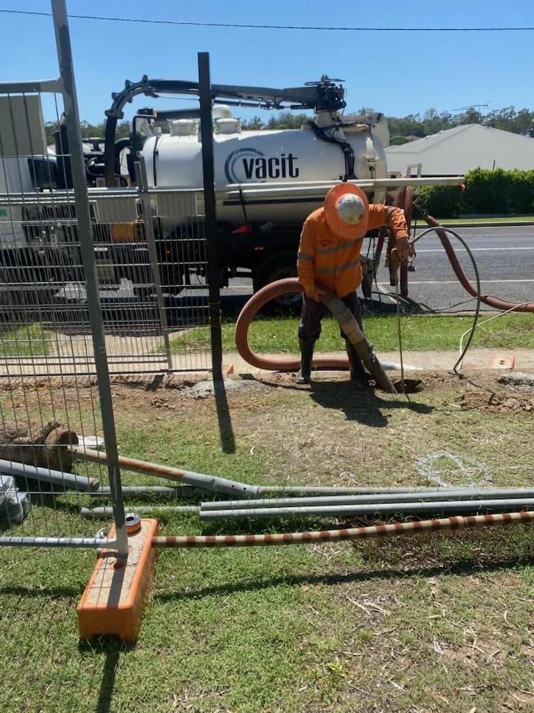 VACIT operator using a vacuum hose beside a branded vacuum truck